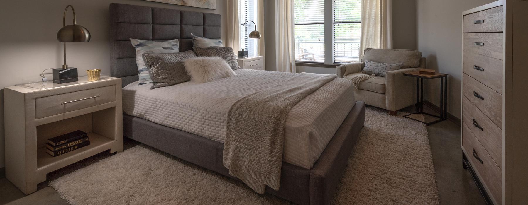 a bedroom with a bed dresser lamps side table and window
