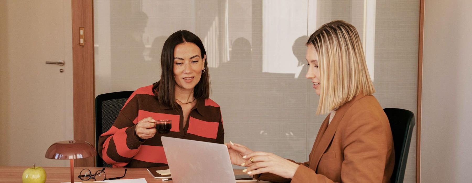 Two women at a desk looking at a laptop.